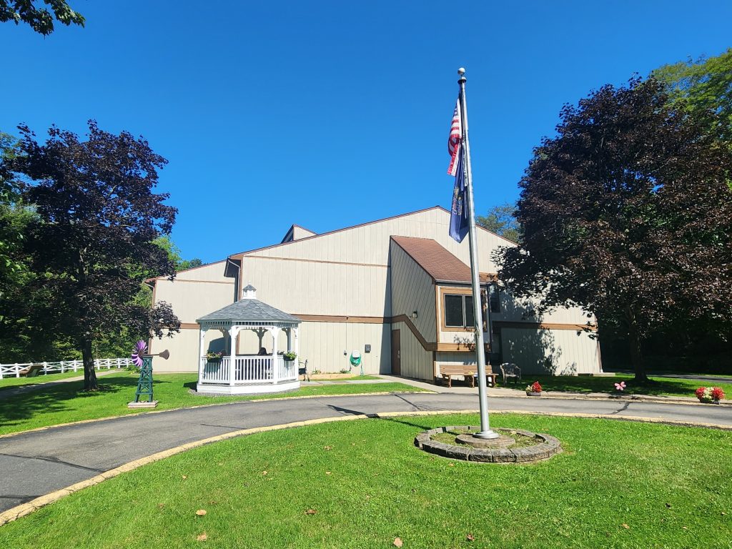 A building with an American flag in front. The building is surrounded by trees and a well kept lawn.